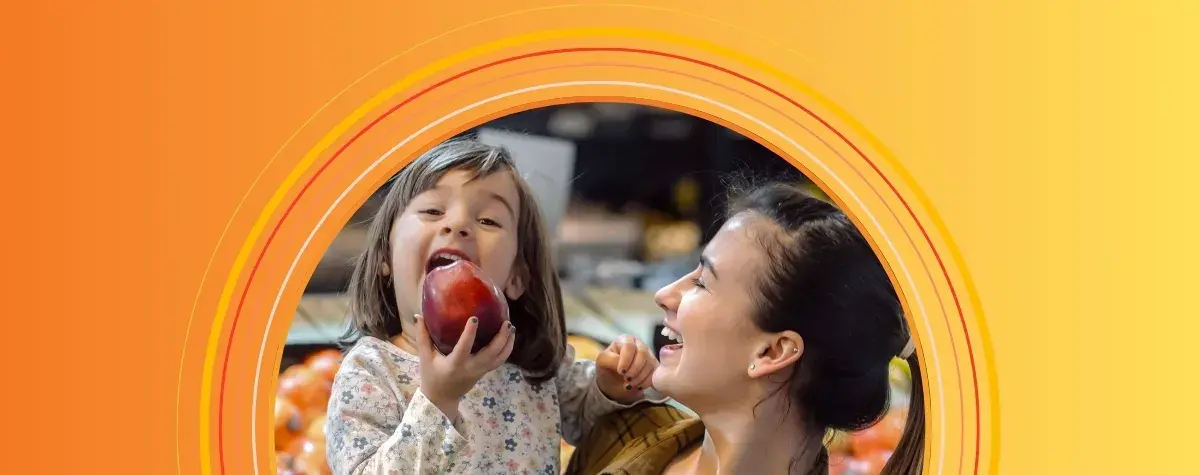 Smiling mom holding young girl about to take a big bite of an apple
