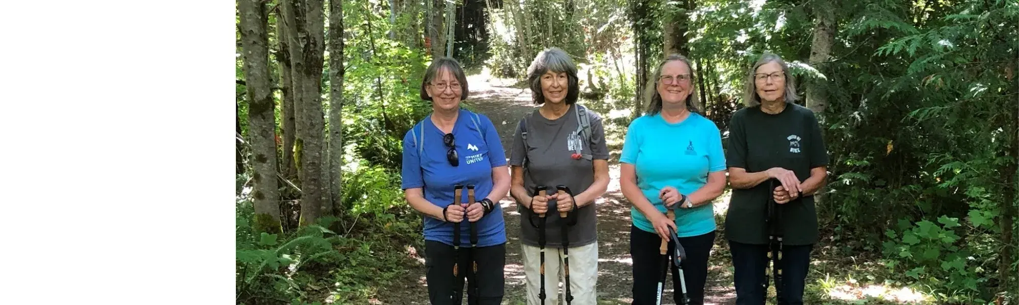 four smiling older women standing on a trail in the woods