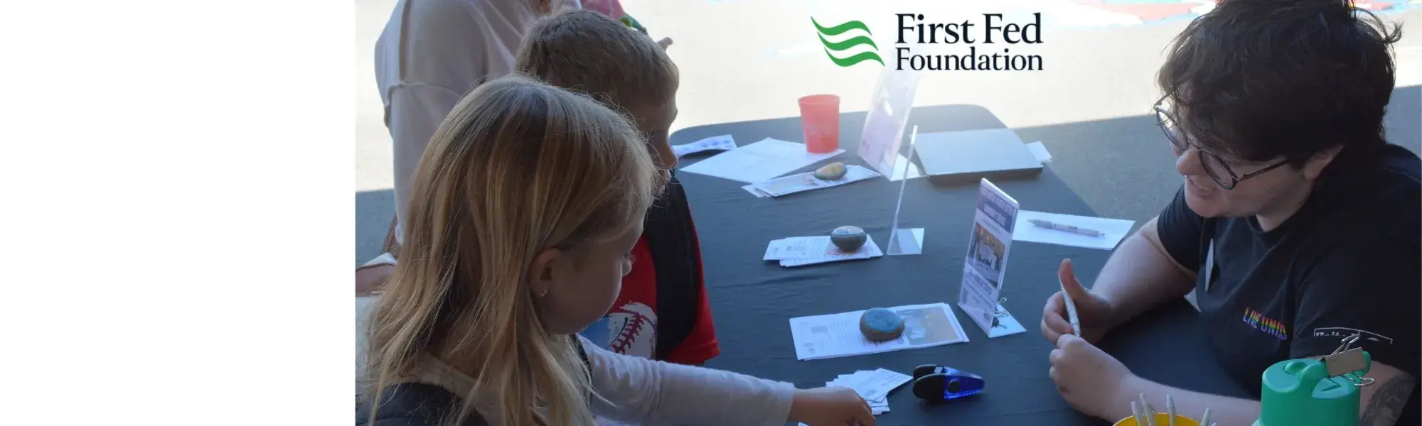 children gathered around a table while an adult talks at an informational fair