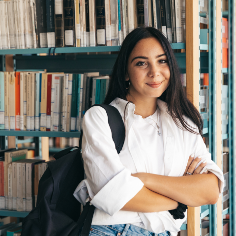 Woman with arms crossed in front of a rack of books