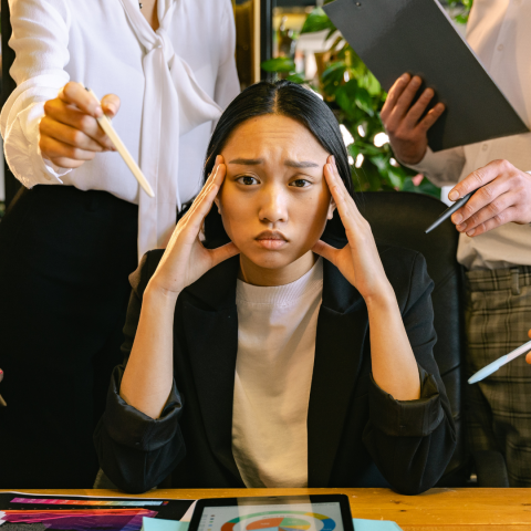 Asian woman looking pained while white people appear to berate her