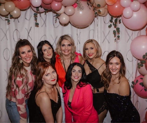 Group of women in cocktail attire posing under a balloon garland