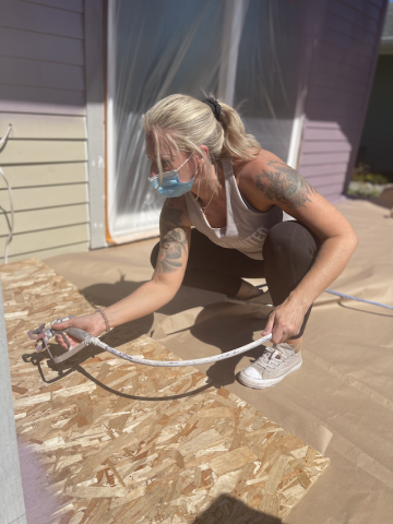 Woman crouching a spraying a house with paint