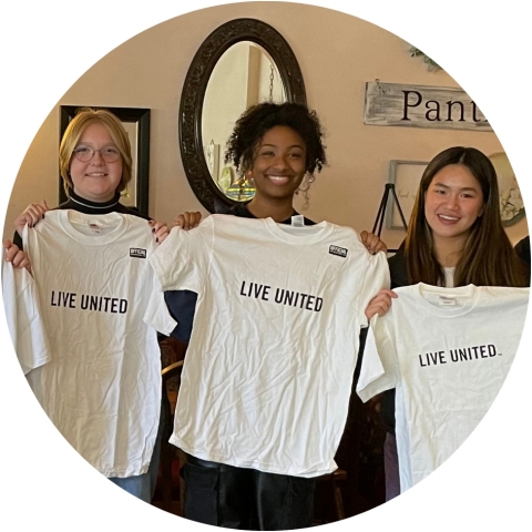 Three teenagers holding up white shirts that read Live United