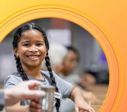 Young girl in long braids handing someone a can of canned food 