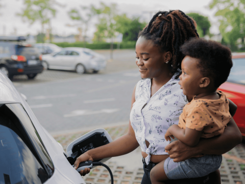 A woman pumping gas while holding a toddler on her hip