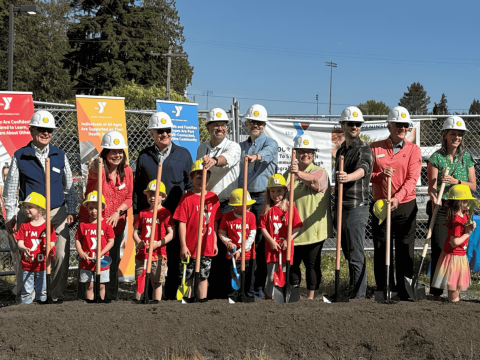 a row of adults and children holding shovels at a ground breaking
