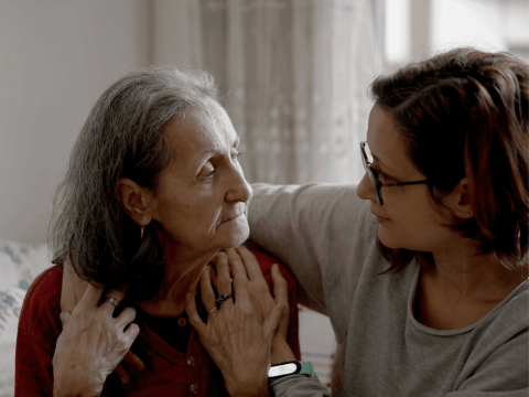 An elderly woman and a younger woman embracing and looking at each other