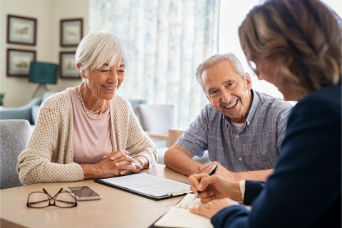 an elderly couple smiling and filling out paperwork with a third person