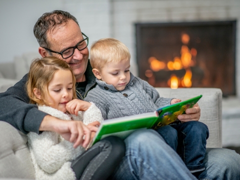 grandpa reading to two young grandchildren near a fireplace