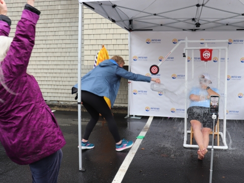 a woman hitting a bullseye and dumping a bucket of water on a seated man