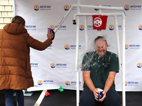 a woman hitting a bullseye and dumping a bucket of water on a seated man