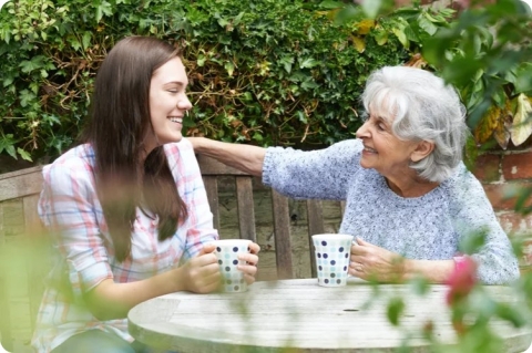 a young woman and an elderly woman with coffee mugs outside