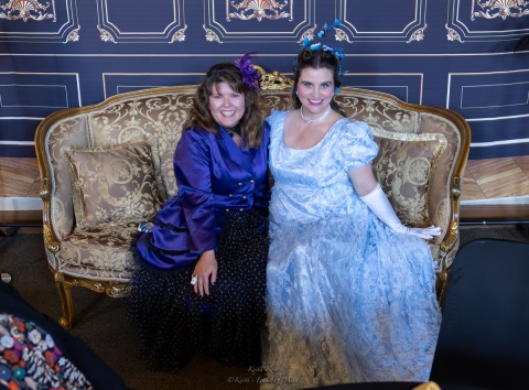 2 women in old fashioned gowns sitting on an antique couch