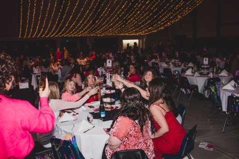 Large room full of round tables with one table of women toasting wine glasses