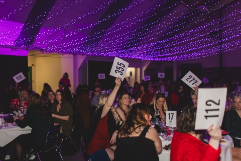 Women holding up bid signs in a large room with purple twinkle lights