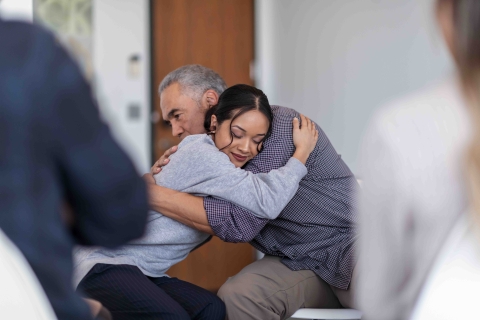 man and woman hugging in circle of people perhaps in a support meeting