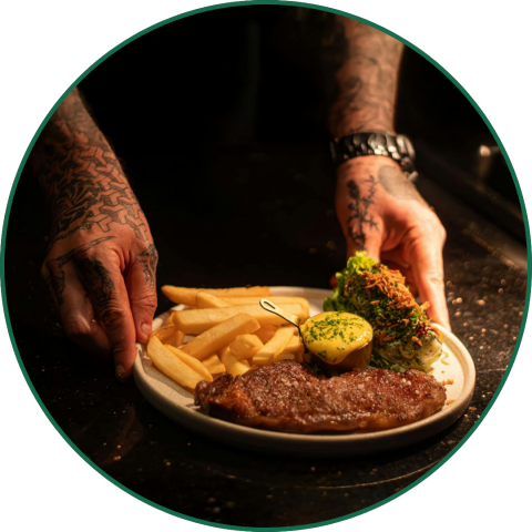 tattooed hands putting a plate of steak down on a table