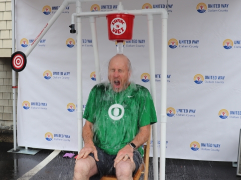 a man sitting in a contraption that dunks a bucket of water on his head