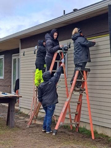 People on ladders applying siding to a house under construction 