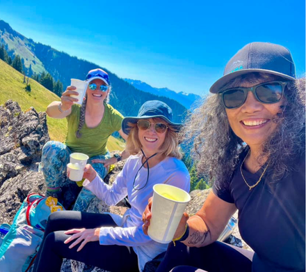 Three women drinking from cups on a mountain top